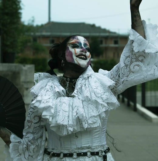 Foto del drag moster "Inu", ha un trucco marcato, bianco e nero, capelli raccolti in due trecce alte, vestito bianco con merletti